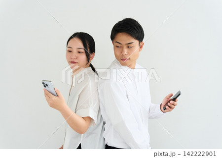 背中合わせでスマートフォンを操作する男女 142222901