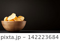 Rustic Potato Chips in a Wooden Bowl with Raw Potatoes Beside 142223684
