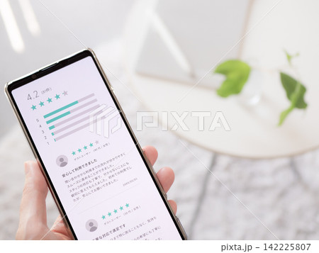 利用サービスの口コミや商品レビューが表示されたスマートフォンの手元写真(スマホ画面はオリジナル制作) 利用サービスの口コミや商品レビューが表示されたスマートフォンの手元写真(スマホ画面はオリジナル制作) 142225807