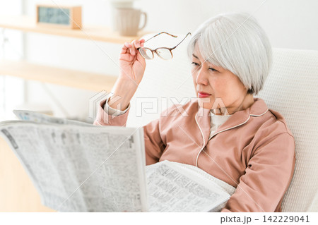 老眼,視力低下で新聞の文字を読むためにメガネを外すグレイヘアのシニア女性 老眼,視力低下で新聞の文字を読むためにメガネを外すグレイヘアのシニア女性 142229041