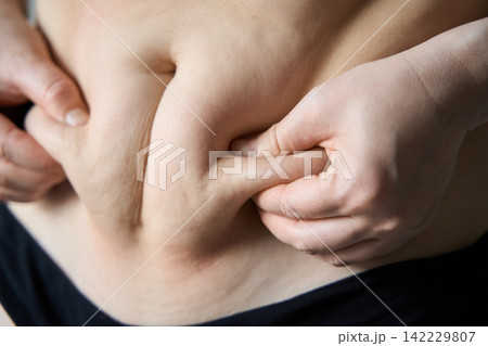 Adult Woman Pinching Abdominal Fat On Bare Torso In Close Up Studio Setting Adult Woman Pinching Abdominal Fat On Bare Torso In Close Up Studio Setting 142229807