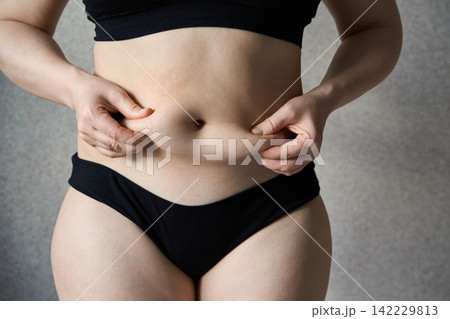 Adult Woman Pinching Abdominal Fat On Torso In Black Underwear Against Neutral Gray Studio Adult Woman Pinching Abdominal Fat On Torso In Black Underwear Against Neutral Gray Studio 142229813