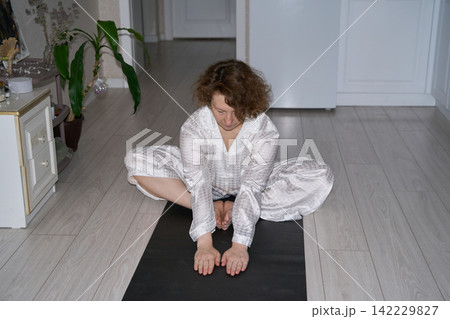 Woman Leaning Forward In Butterfly Stretch With Hands Holding Feet While Seated On Black Exercise Woman Leaning Forward In Butterfly Stretch With Hands Holding Feet While Seated On Black Exercise 142229827