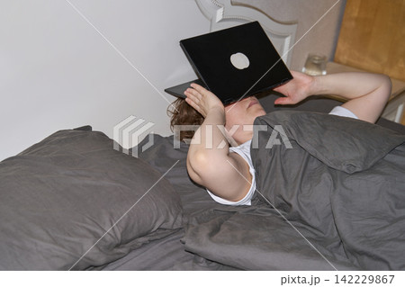 Woman Lying Under Gray Blanket With Open Laptop Covering Face In Bedroom, Expressing Digital 142229867