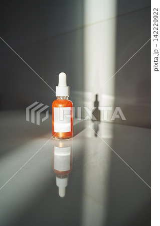 Dropper Bottle With Orange Serum Standing On Reflective Surface In Studio Setting Lit By Narrow Dropper Bottle With Orange Serum Standing On Reflective Surface In Studio Setting Lit By Narrow 142229922
