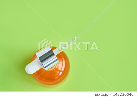Dropper Resting On Top Of Orange Serum Bottle On Green Background In Studio Flatlay Top View 142230040