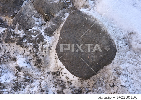 Rounded Rock Partially Exposed In Patchy Snow On Ground At Cold Outdoor Scene Showing Gritty Frozen Rounded Rock Partially Exposed In Patchy Snow On Ground At Cold Outdoor Scene Showing Gritty Frozen 142230136