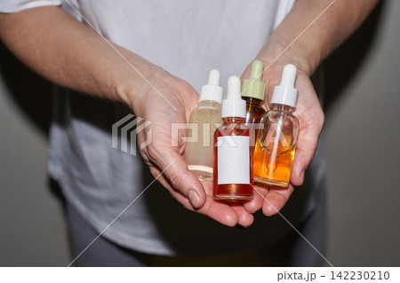 Pair Of Hands Holding Five Glass Dropper Bottles Showing Colored Serums In Indoor Neutral Setting 142230210