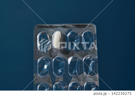 Single White Tablet Centered In Mostly Empty Blister Pack Laying Flat On Dark Blue Background 142230275
