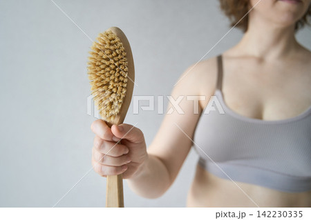 Woman Holding Natural Body Brush Upright In Minimalist Indoor Setting With Neutral Wall And Cropped 142230335