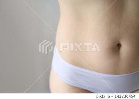 Female Abdomen In White Underwear Shown In Close-Up Against Plain Indoor Background With Soft Female Abdomen In White Underwear Shown In Close-Up Against Plain Indoor Background With Soft 142230454
