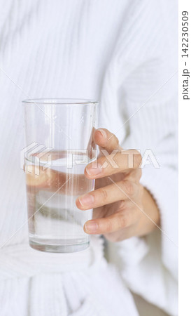Hand Holding Glass Of Water Wearing White Robe Indoors Bathroom Or Bedroom Setting Closeup Showing 142230509