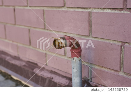 Exposed Water Pipe Elbow Protruding From Pink Brick Wall Outdoors Closeup Showing Rusted Fitting 142230729