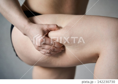 Adult Woman Pinching Thigh Fat In Side View Against Plain Studio Background 142230730