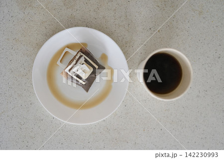 Drip Coffee Bag Positioned On White Plate Beside Paper Cup Of Black Coffee On Speckled Countertop Drip Coffee Bag Positioned On White Plate Beside Paper Cup Of Black Coffee On Speckled Countertop 142230993