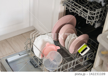 Open Dishwasher Lower Rack Filled With Pink Plates White Bowls And Plastic Cups In White Kitchen Open Dishwasher Lower Rack Filled With Pink Plates White Bowls And Plastic Cups In White Kitchen 142231109