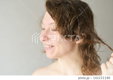 Young Woman With Wet Curly Hair Smiling With Eyes Closed While Holding A Strand In Neutral Indoor Young Woman With Wet Curly Hair Smiling With Eyes Closed While Holding A Strand In Neutral Indoor 142231190