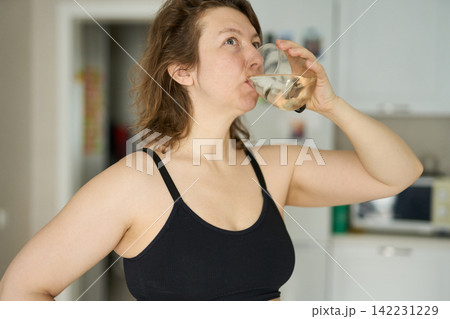 Woman Tilting Head Back While Drinking From Glass In Kitchen Near Cabinets Microwave Woman Tilting Head Back While Drinking From Glass In Kitchen Near Cabinets Microwave 142231229