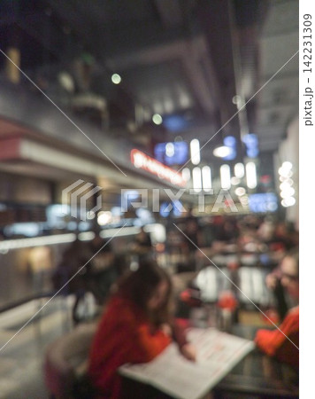 Person Writing At Table In Crowded Indoor Cafeteria With Overhead Lights Blurred Patrons And Modern Person Writing At Table In Crowded Indoor Cafeteria With Overhead Lights Blurred Patrons And Modern 142231309