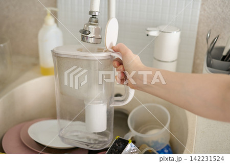 Water Filter Pitcher Being Held Open Under Faucet Over Kitchen Sink With Dishes Soap Dispenser Water Filter Pitcher Being Held Open Under Faucet Over Kitchen Sink With Dishes Soap Dispenser 142231524