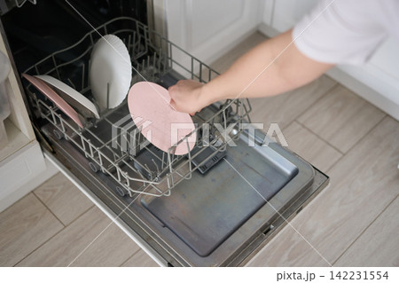 Hand Loading Pink Plate Into Dishwasher Rack Over Lowered Door Showing White And Pink Dishes 142231554