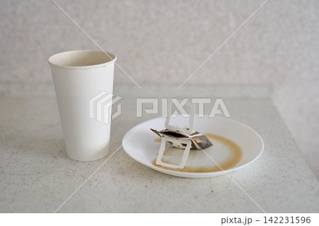 Tea Bag Placed Beside Paper Cup On White Plate With Circular Tea Stain On Speckled Countertop Tea Bag Placed Beside Paper Cup On White Plate With Circular Tea Stain On Speckled Countertop 142231596