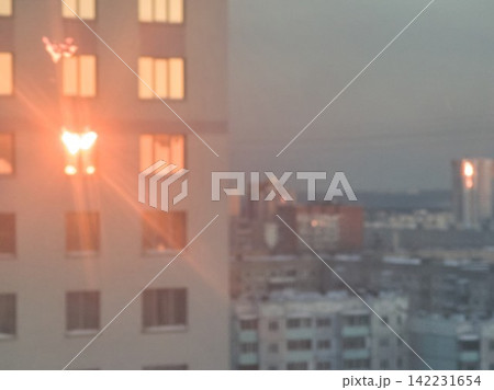 Apartment Building Windows Illuminated Against Hazy Cityscape With Lens Flare And Distant Downtown 142231654