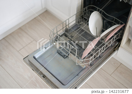 Dishwasher Rack With Pink And White Plates Open And Partially Loaded On Tiled Kitchen Floor Near Dishwasher Rack With Pink And White Plates Open And Partially Loaded On Tiled Kitchen Floor Near 142231677