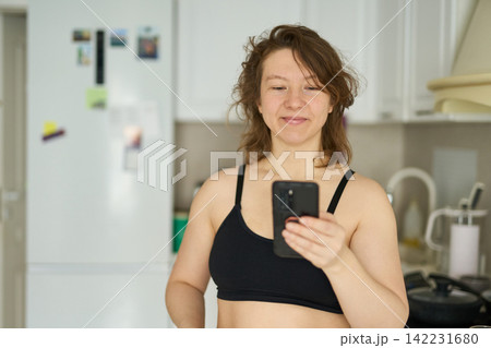 Woman Smiling While Checking Smartphone In Compact Home Kitchen With Refrigerator Cabinets Woman Smiling While Checking Smartphone In Compact Home Kitchen With Refrigerator Cabinets 142231680