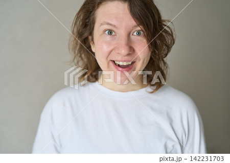 Woman Smiling With Surprised Expression Standing Indoors Against Plain Neutral Background Wearing Woman Smiling With Surprised Expression Standing Indoors Against Plain Neutral Background Wearing 142231703