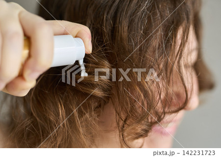 Woman Applying Conditioner To Damp Curly Brown Hair With Pump Bottle In Closeup Indoor Setting 142231723