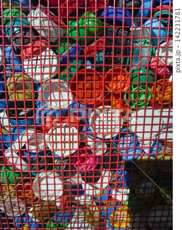 Assorted Plastic Bottle Caps Pressed Against Red Metal Grid Forming Dense Colorful Mosaic 142231781