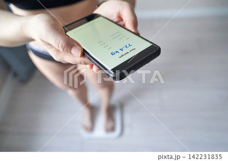 Close View Of Hands Holding Smartphone With Weight Readout As Person Stands On A Scale For Weight Close View Of Hands Holding Smartphone With Weight Readout As Person Stands On A Scale For Weight 142231835