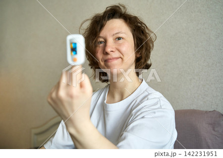 Woman holding pulse oximeter and smiling showing recovery and health monitoring at home Woman holding pulse oximeter and smiling showing recovery and health monitoring at home 142231951
