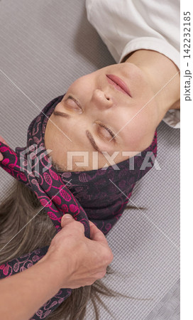 Close Up Of Therapist Hands Adjusting Scarf Around Head Of Relaxed Woman Illustrating Wellness Close Up Of Therapist Hands Adjusting Scarf Around Head Of Relaxed Woman Illustrating Wellness 142232185