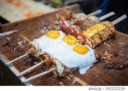 Grilled street food skewers topped fried eggs cheese sauces herbs representing popular Korean market snacks savory fast food Asian cuisine Grilled street food skewers topped fried eggs cheese sauces herbs representing popular Korean market snacks savory fast food Asian cuisine 142232226