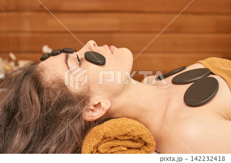 Young Caucasian Female Relaxing With Hot Stone Therapy In A Spa Setting For Relaxation And Wellness Young Caucasian Female Relaxing With Hot Stone Therapy In A Spa Setting For Relaxation And Wellness 142232418