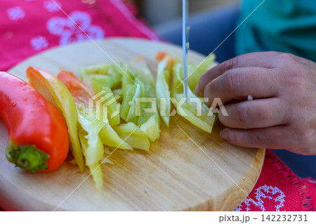 Person slicing a fresh red and green bell pepper on a wooden cutting board Person slicing a fresh red and green bell pepper on a wooden cutting board 142232731