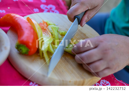 Person slicing a fresh red and green bell pepper on a wooden cutting board 142232732