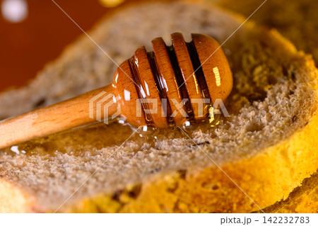 Golden honey and fresh bread slices beside glass jar in warm rustic kitchen setting Golden honey and fresh bread slices beside glass jar in warm rustic kitchen setting 142232783