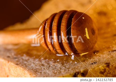 Golden honey and fresh bread slices beside glass jar in warm rustic kitchen setting Golden honey and fresh bread slices beside glass jar in warm rustic kitchen setting 142232785