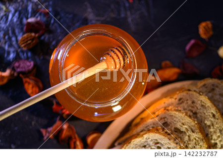 Golden honey and fresh bread slices beside glass jar in warm rustic kitchen setting Golden honey and fresh bread slices beside glass jar in warm rustic kitchen setting 142232787