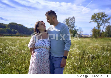 mature couple expecting baby posing together in wild flower meadow in summer mature couple expecting baby posing together in wild flower meadow in summer 142234391