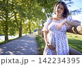 pregnant mature woman in floral dress walking on sunny rural pathway 142234395