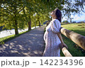 pregnant mature woman in floral dress walking on sunny rural pathway 142234396