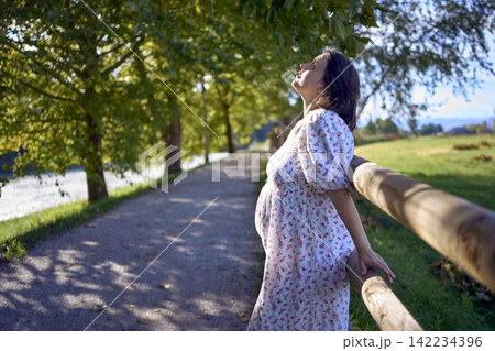 pregnant mature woman in floral dress walking on sunny rural pathway pregnant mature woman in floral dress walking on sunny rural pathway 142234396