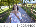 pregnant mature woman in floral dress walking on sunny rural pathway 142234400
