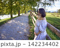 pregnant mature woman in floral dress walking on sunny rural pathway 142234402