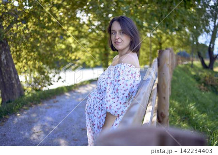 pregnant mature woman in floral dress walking on sunny rural pathway pregnant mature woman in floral dress walking on sunny rural pathway 142234403