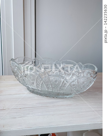 Large decorative crystal glass bowl with intricate patterns resting on a rustic wooden table indoors, elegant tableware piece catching soft light in a bright home interior setting for display 142235630